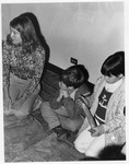 Children sitting on the floor, one holding a hide scraper by Dan Wooley